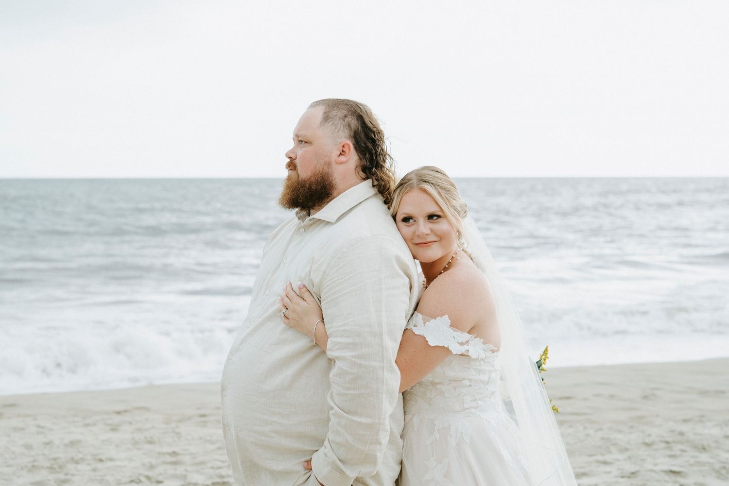 A couple embraces on a beach with ocean waves in the background during their romantic photoshoot.