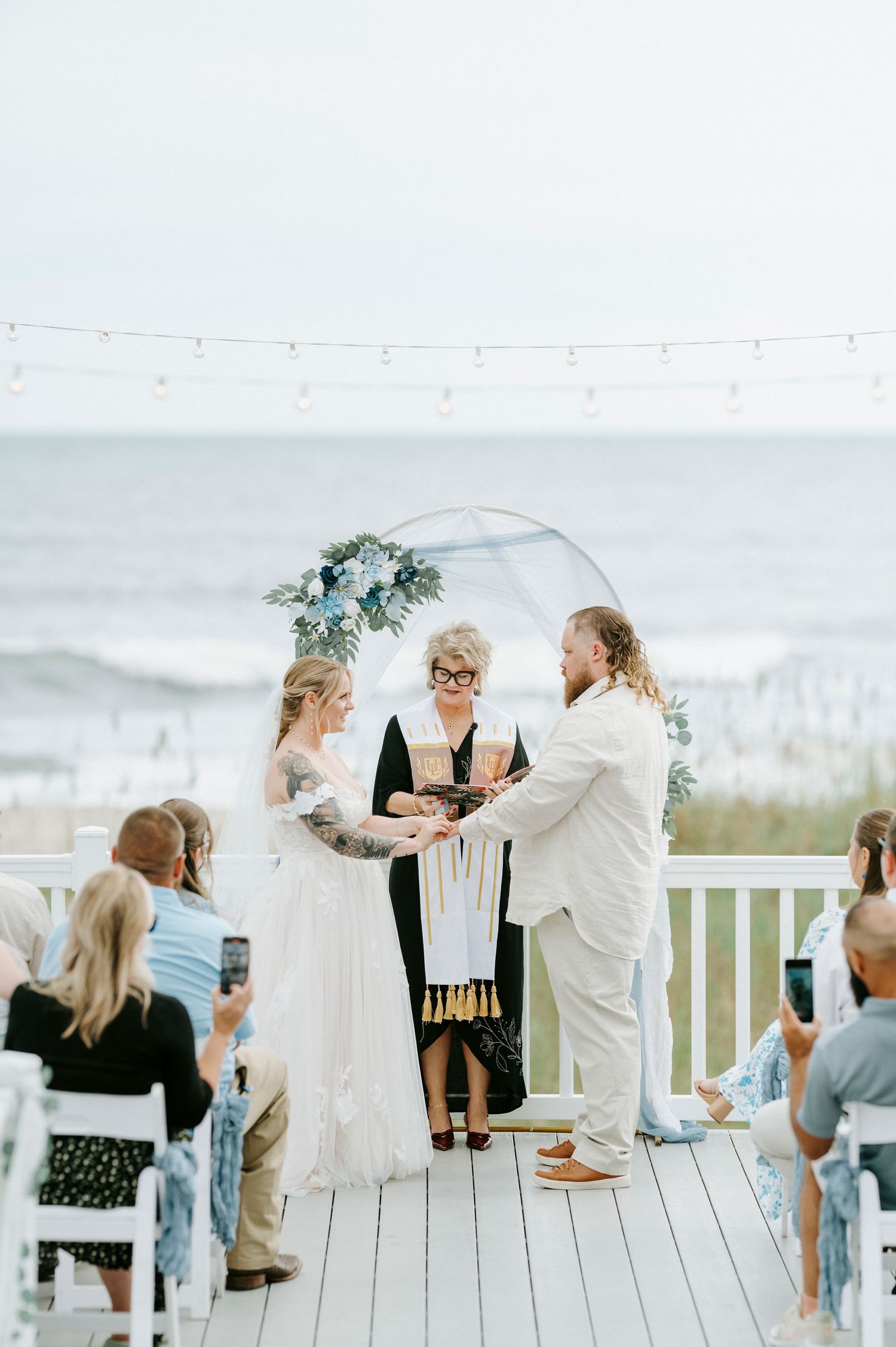 Wedding guests gather on a white deck overlooking the ocean to celebrate during an intimate outdoor ceremony.