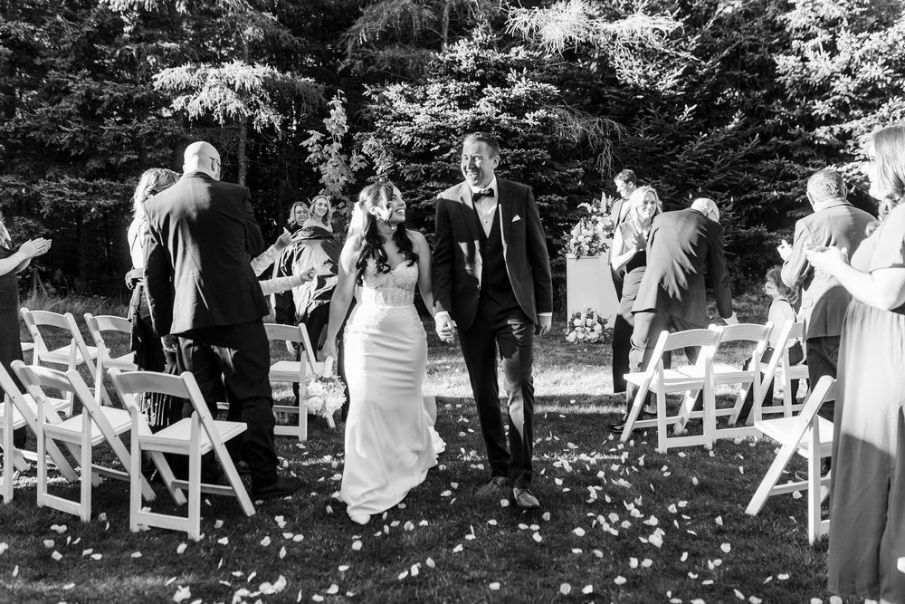Wedding guests toss white flower petals during an outdoor garden ceremony celebration.