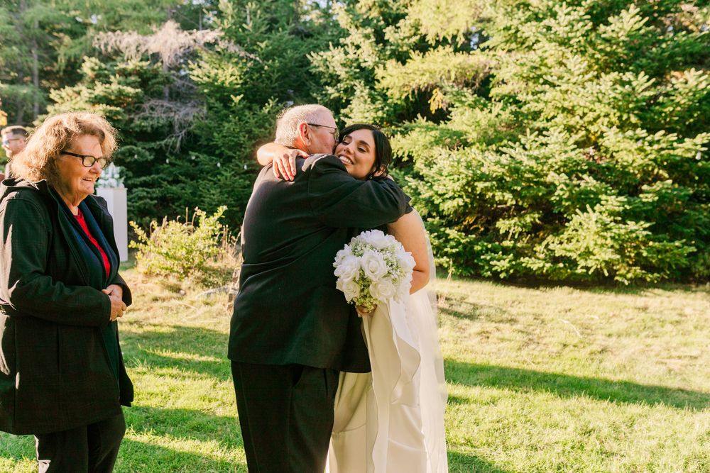 A wedding couple and their party share joyful moments in a sunny garden setting with lush green foliage.