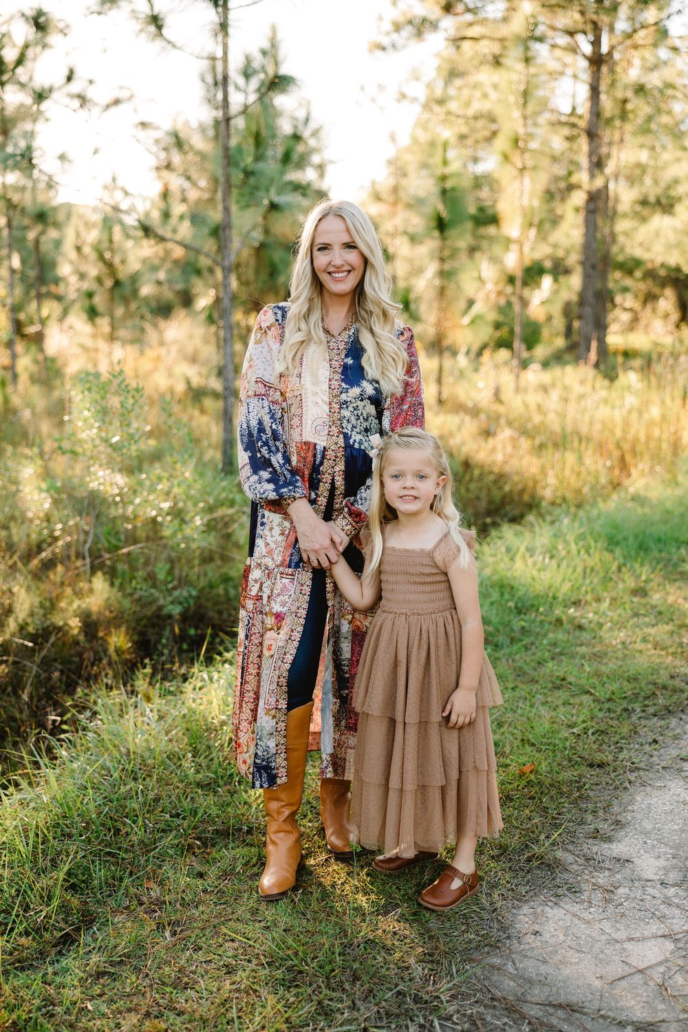 A parent and child pose together on a nature trail wearing coordinated fall outfits with brown and floral patterns.