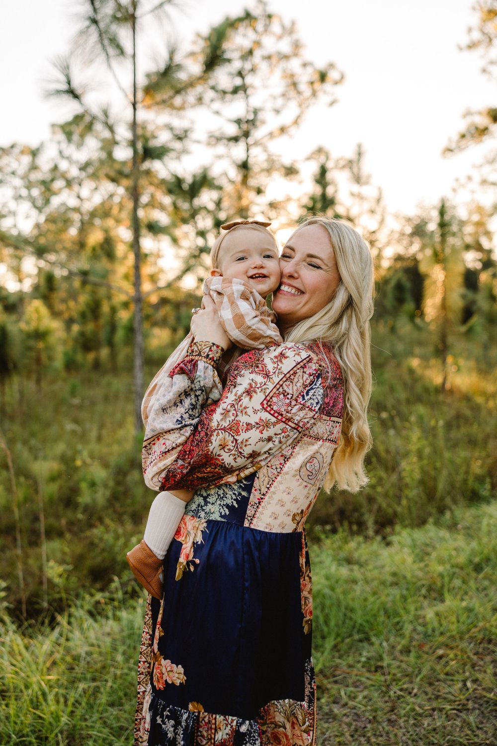 Mother and child share joyful laughter together while playing outdoors in a natural setting at sunset.