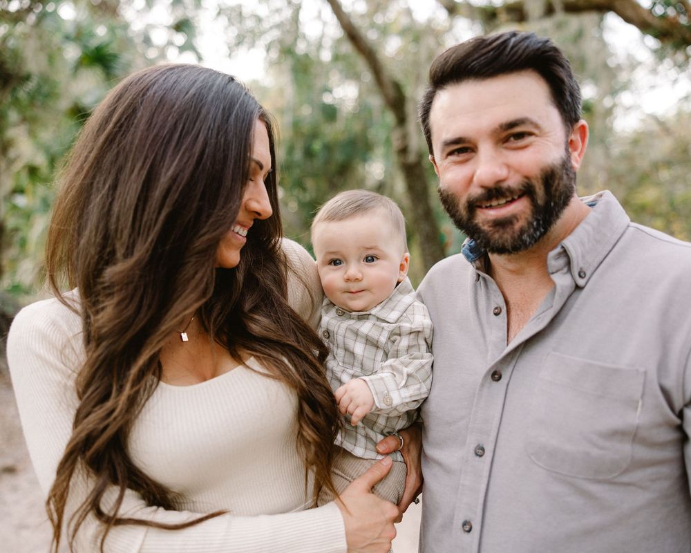 Family wearing neutral tones poses together outdoors in a natural setting during golden hour.
