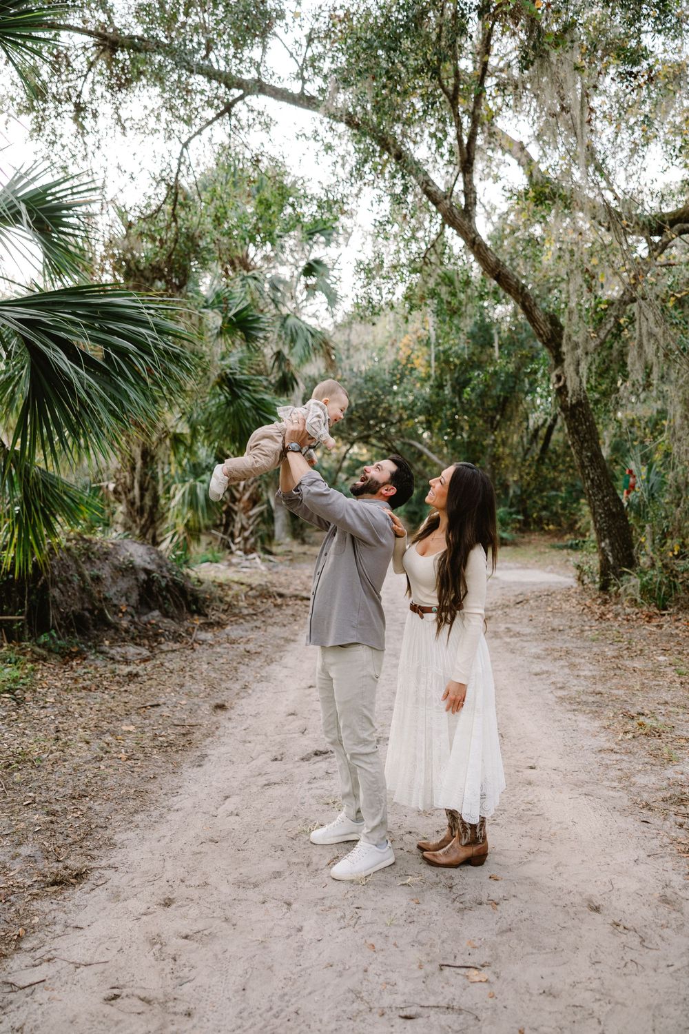 A couple shares a romantic moment on a sandy path surrounded by lush tropical foliage and palm trees.