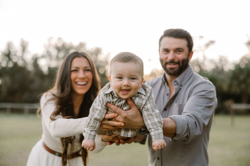 A family enjoys outdoor portraits with their dog in a grassy field at sunset.