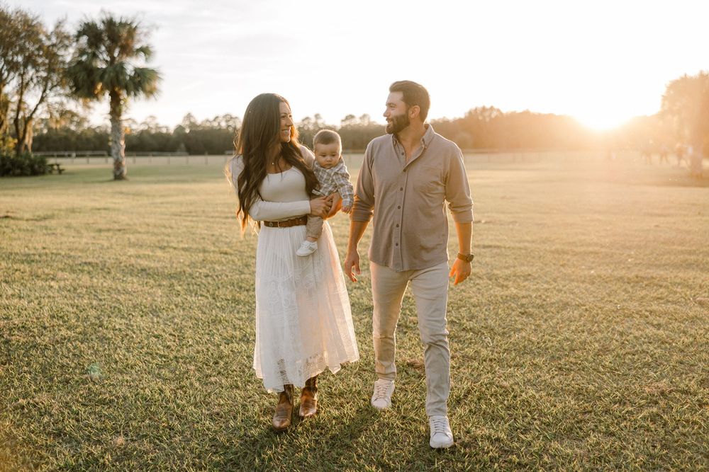 A couple walks hand in hand through a grassy field at sunset creating a romantic silhouette against the golden sky.