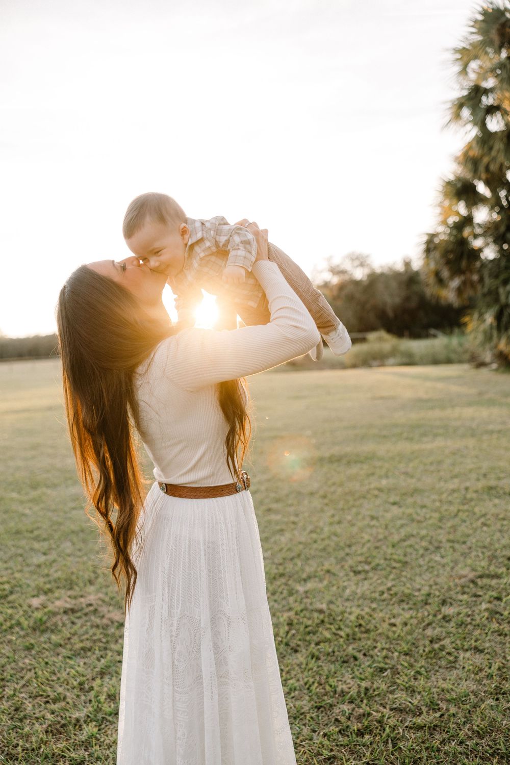 A person in a flowing white dress twirls in a grassy field at sunset creating a dreamy silhouette effect.