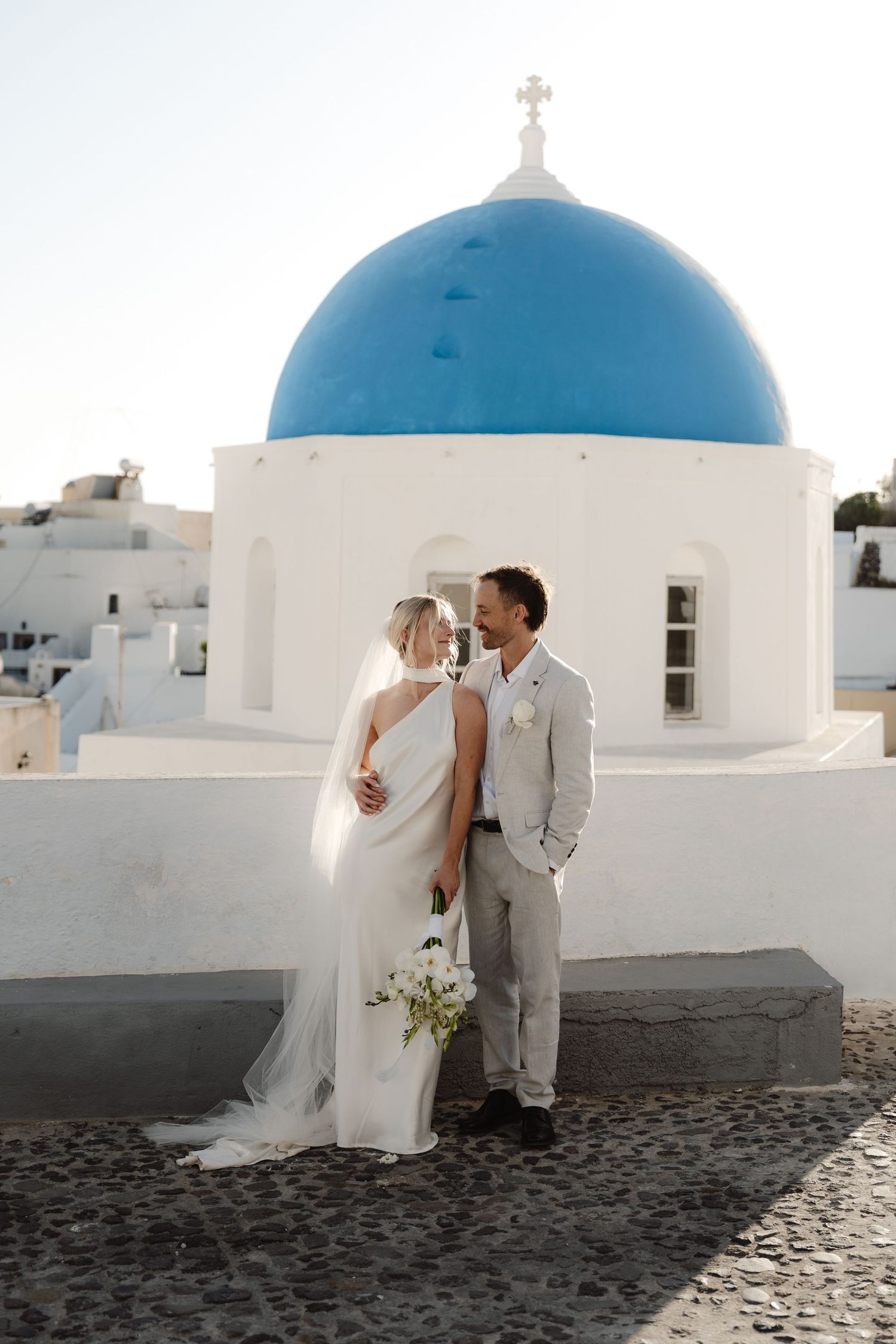 A modern editorial wedding photo of a Mornington peninsula couple who had an elopement in Santorini standing infront of blue domes