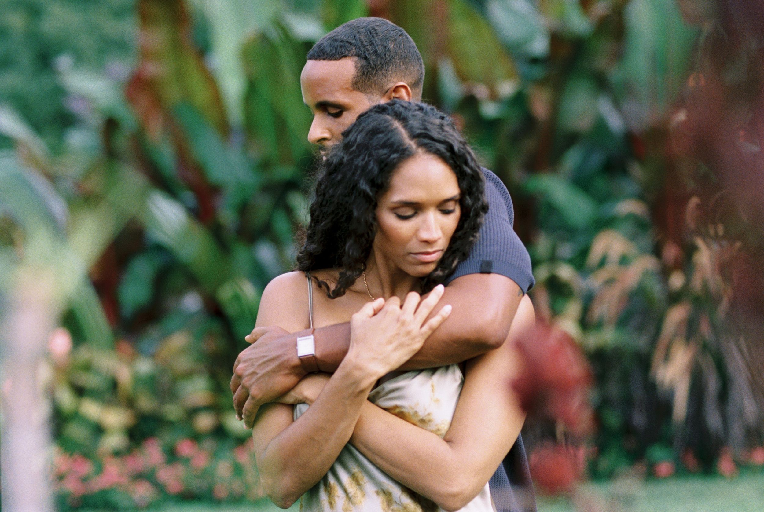 A couple embraces tenderly in a lush green garden setting during an intimate outdoor photo session.