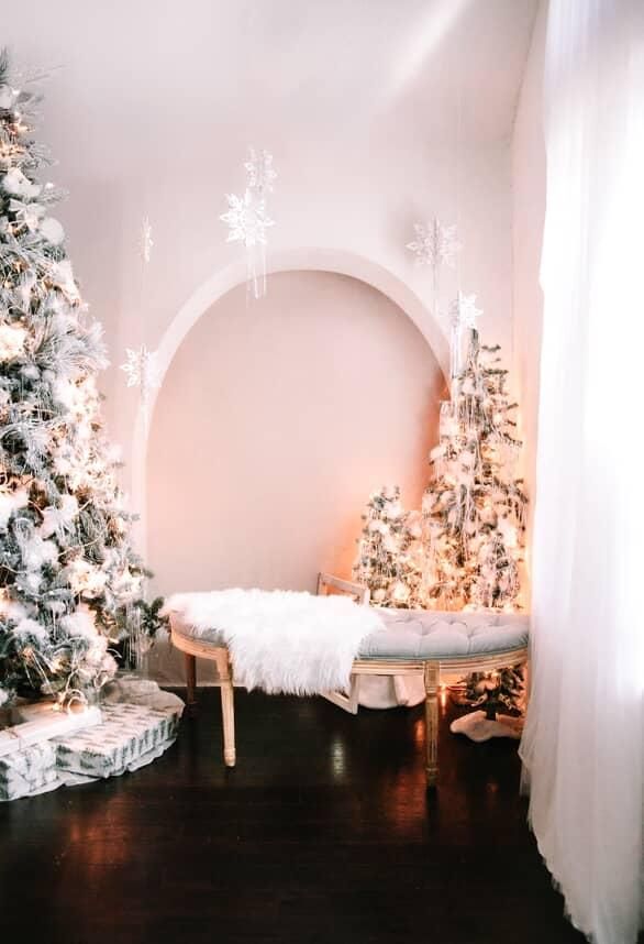 A cozy winter scene with illuminated white Christmas trees and soft lighting in an arched interior space.