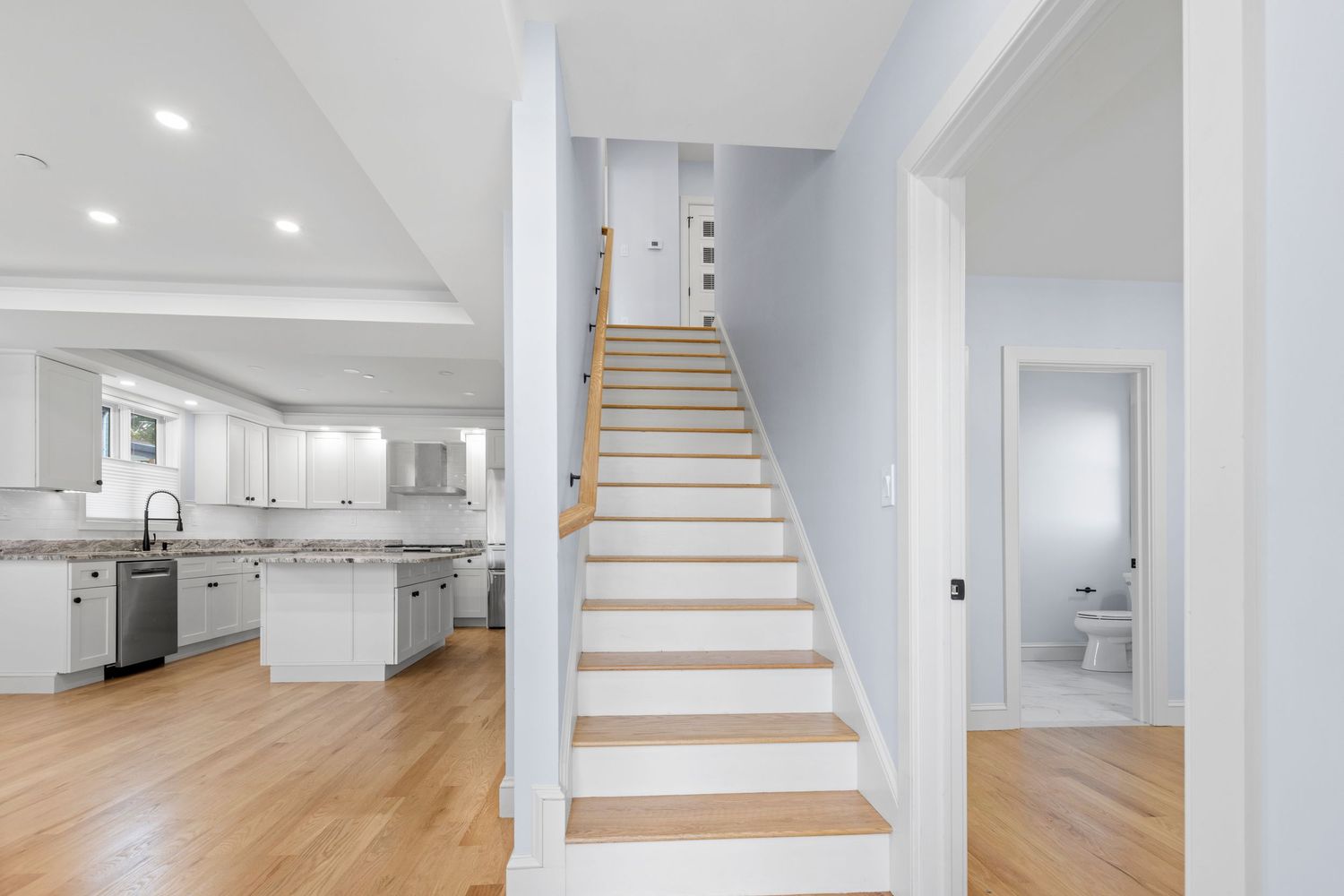 Modern staircase with light wood steps leading to upper floor with white kitchen visible in background.