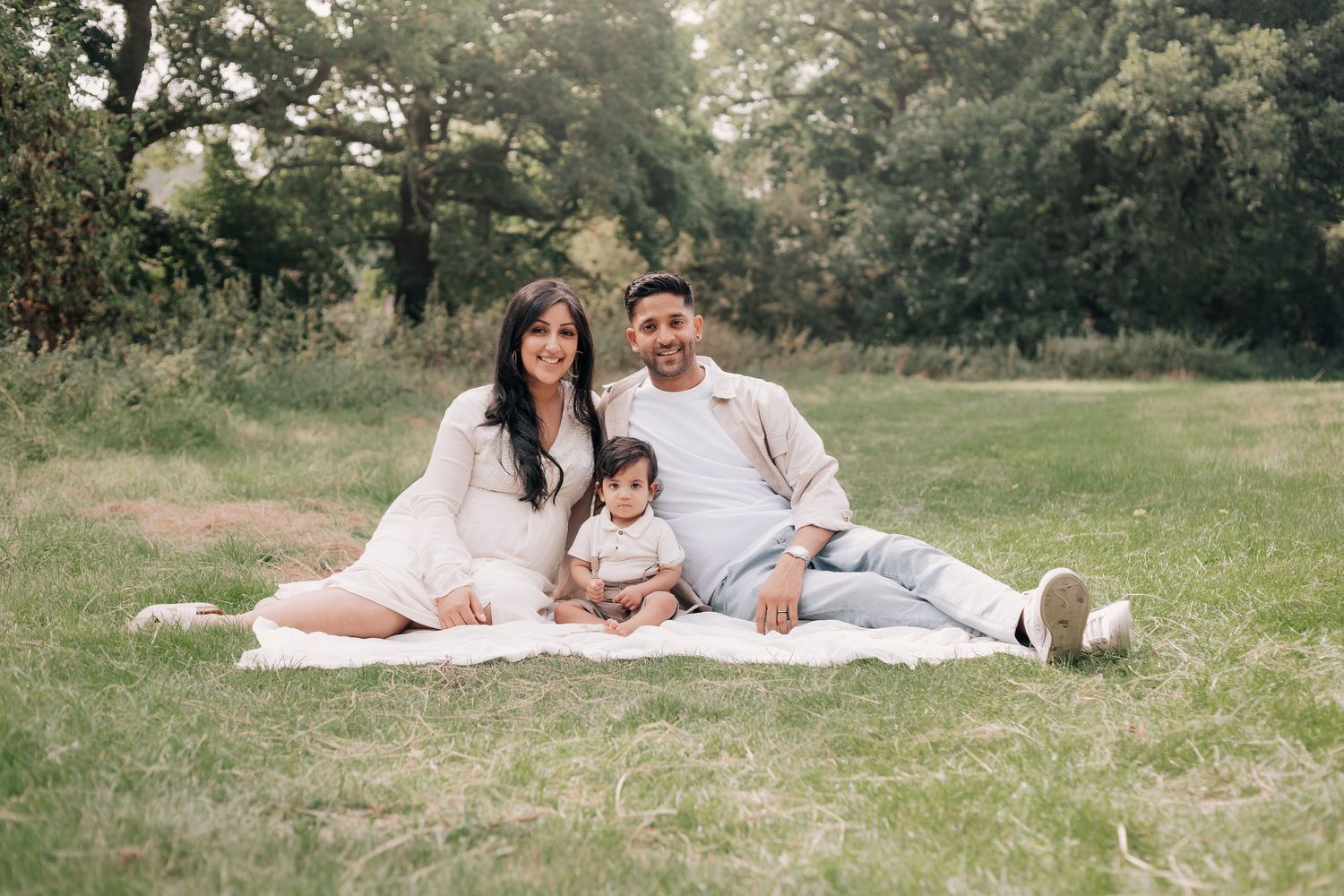 Family lounging on white blanket during outdoor photo session in park.