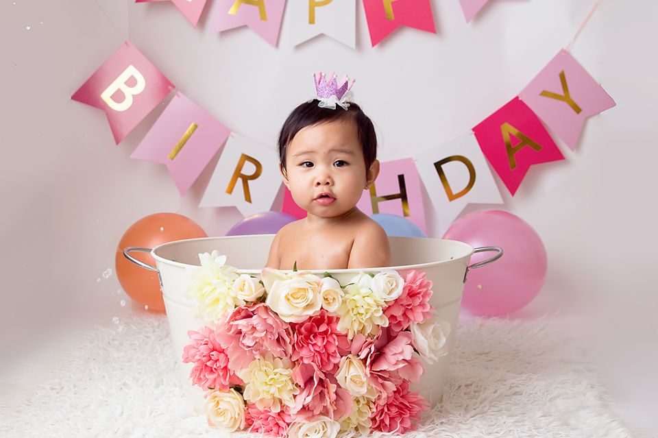 Baby in decorated bathtub with pink and cream flowers for birthday photoshoot.