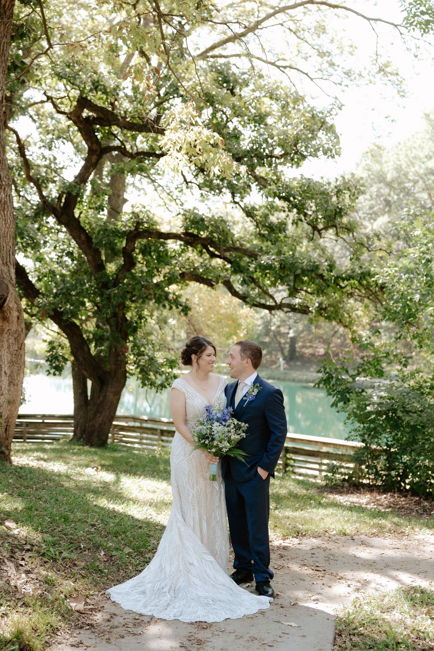 A couple shares an intimate moment under blooming trees in a rustic outdoor setting during their wedding.