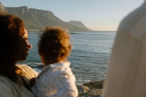 People enjoying a scenic coastal view with mountains and ocean on a sunny day.