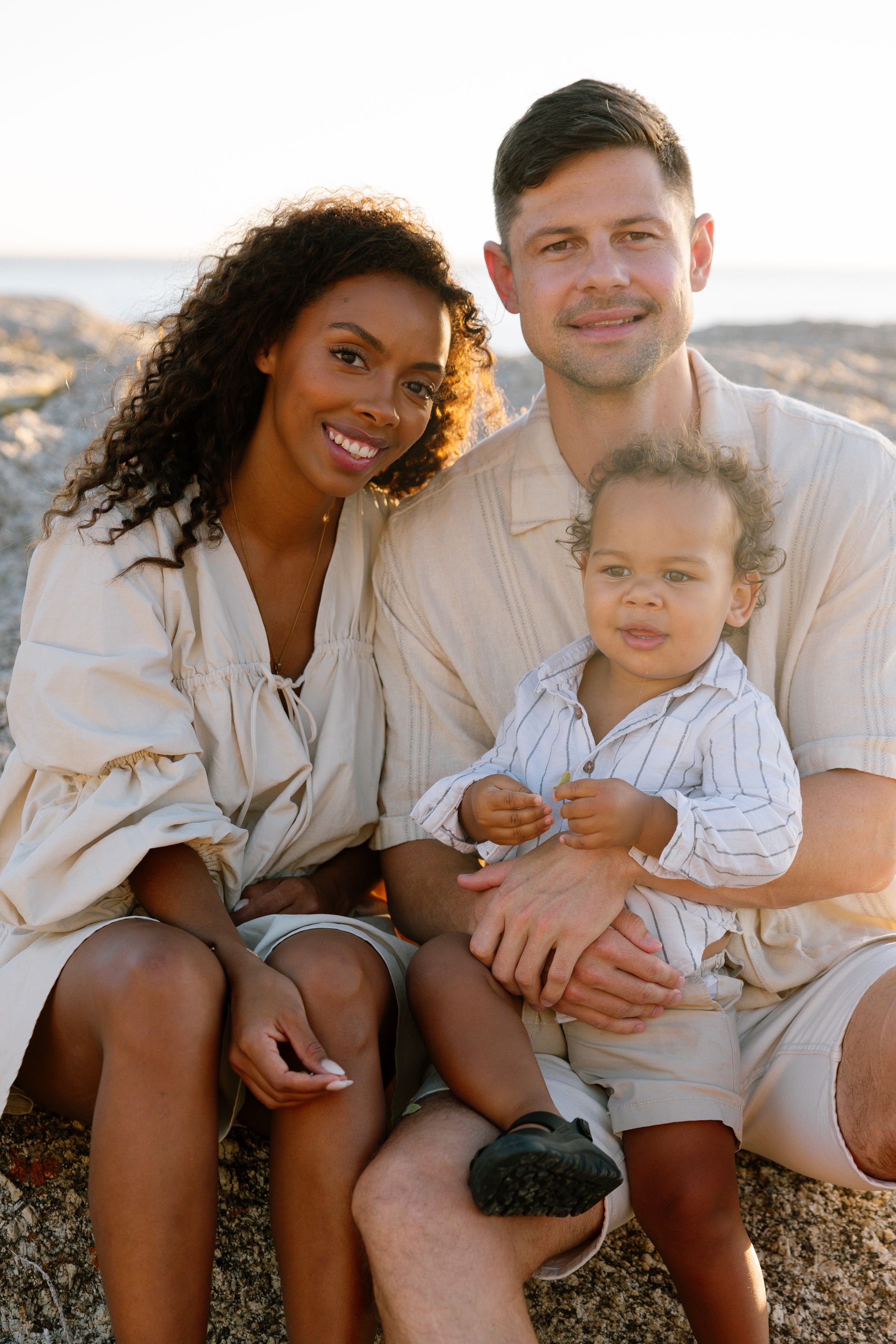 A family wearing white and beige clothing sits together outdoors during golden hour.