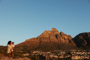 Two figures stand together overlooking Cape Town with Table Mountain glowing orange in sunset light.