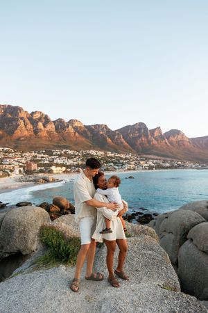 A scenic view of Camps Bay beach in Cape Town with dramatic mountain peaks and coastal rocks at sunset.
