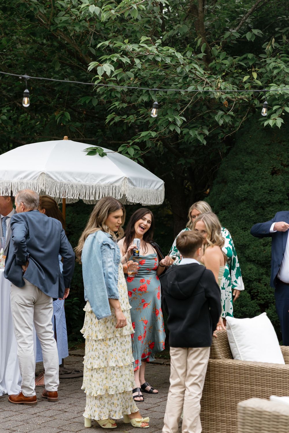 Garden party guests mingling under decorative white umbrellas among lush greenery.
