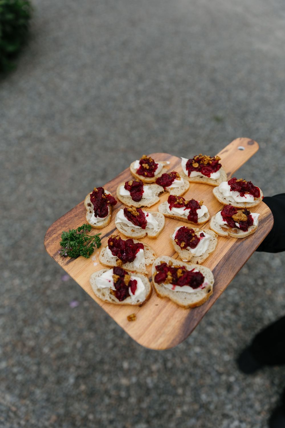 Wooden serving board with appetizers topped with whipped cream and cranberries arranged in a row.