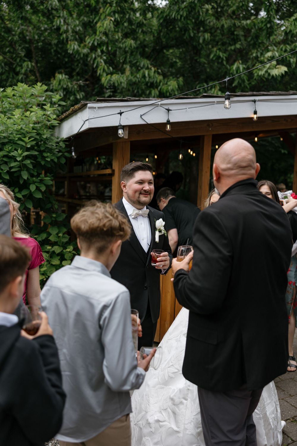 Wedding guests gather around a rustic wooden booth outdoors during a celebration.