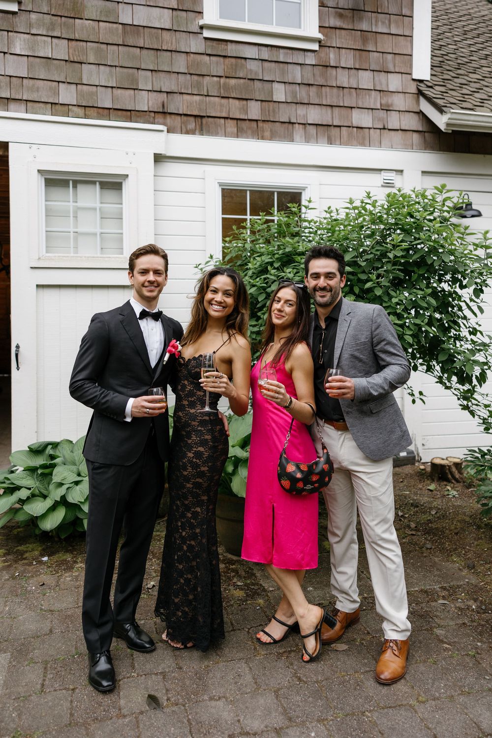 Four people pose together at a casual outdoor gathering against a shingled wall.