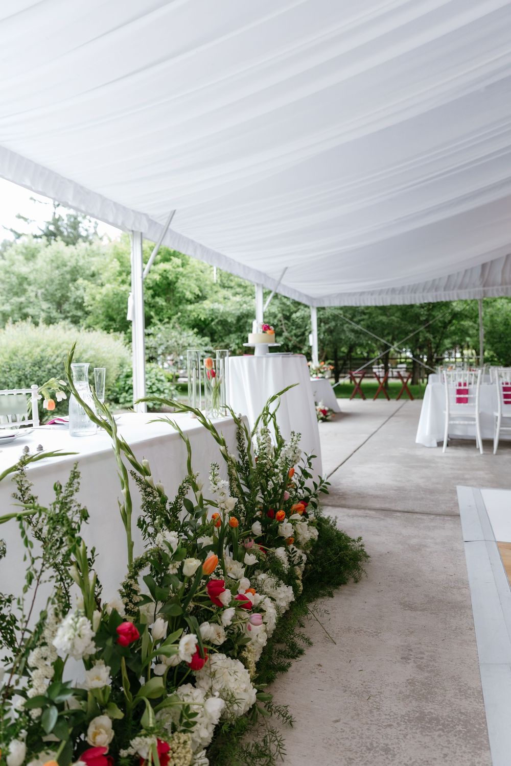 White tent canopy decorated with elegant floral arrangements featuring red and white flowers along a gravel pathway.