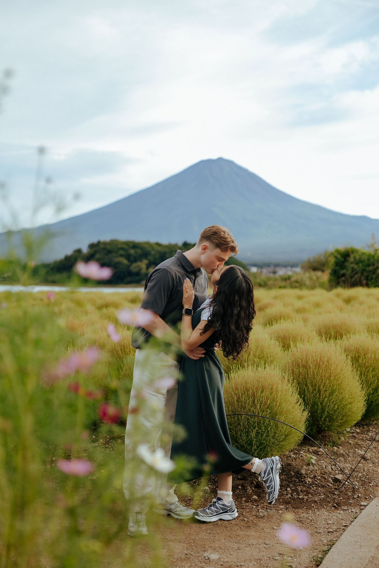 A couple shares a romantic moment on a mountain trail with majestic Mount Fuji peak rising in the background.