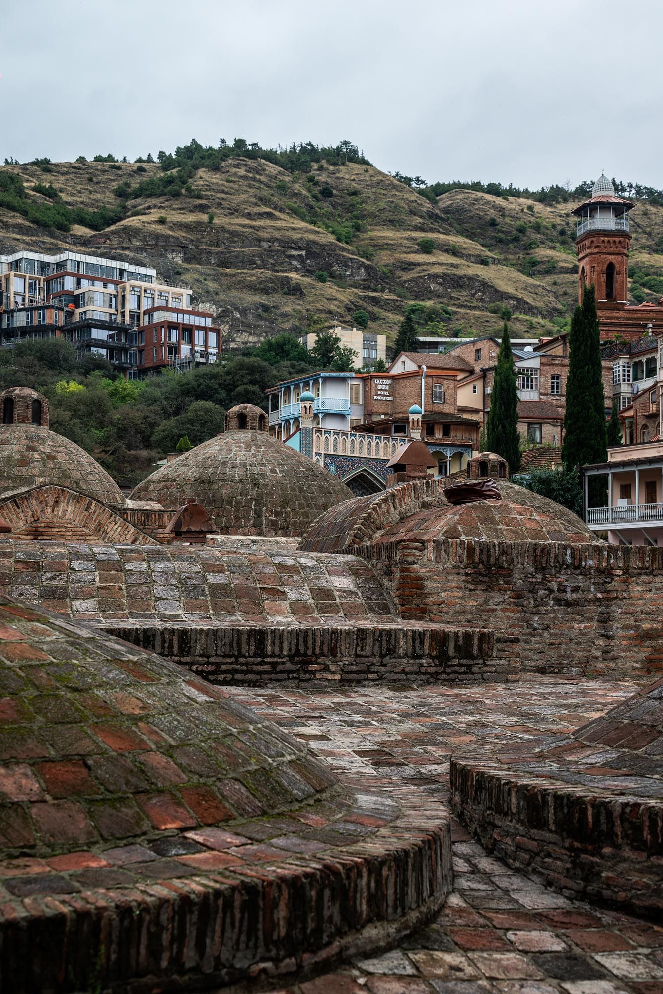 Historic sulfur baths with domed roofs in Tbilisi's old town with traditional architecture and hillside buildings in background.