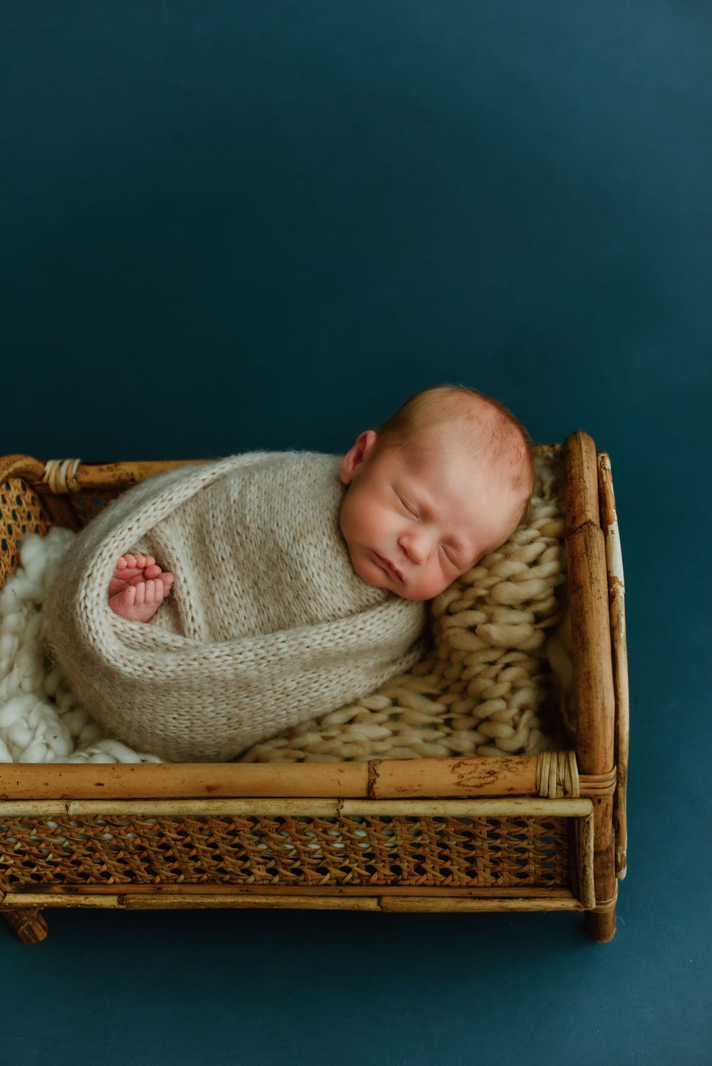 Newborn baby swaddled in beige wrap sleeping in vintage wooden bed frame.