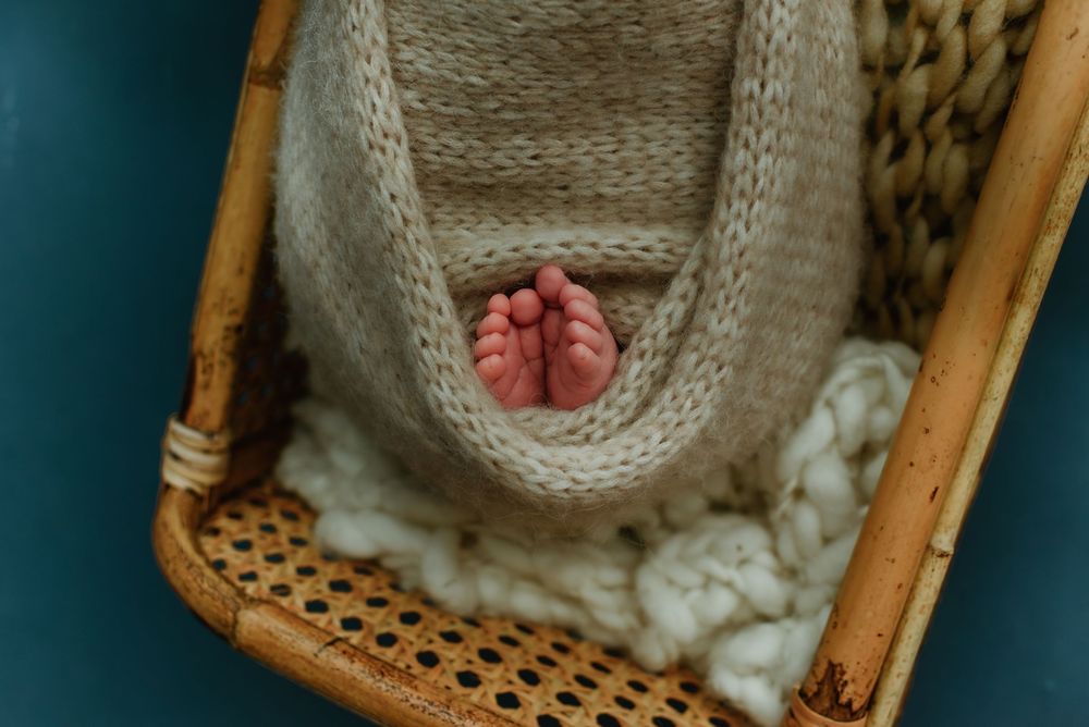 Newborn baby sleeping peacefully in vintage wicker basket with knit blanket.