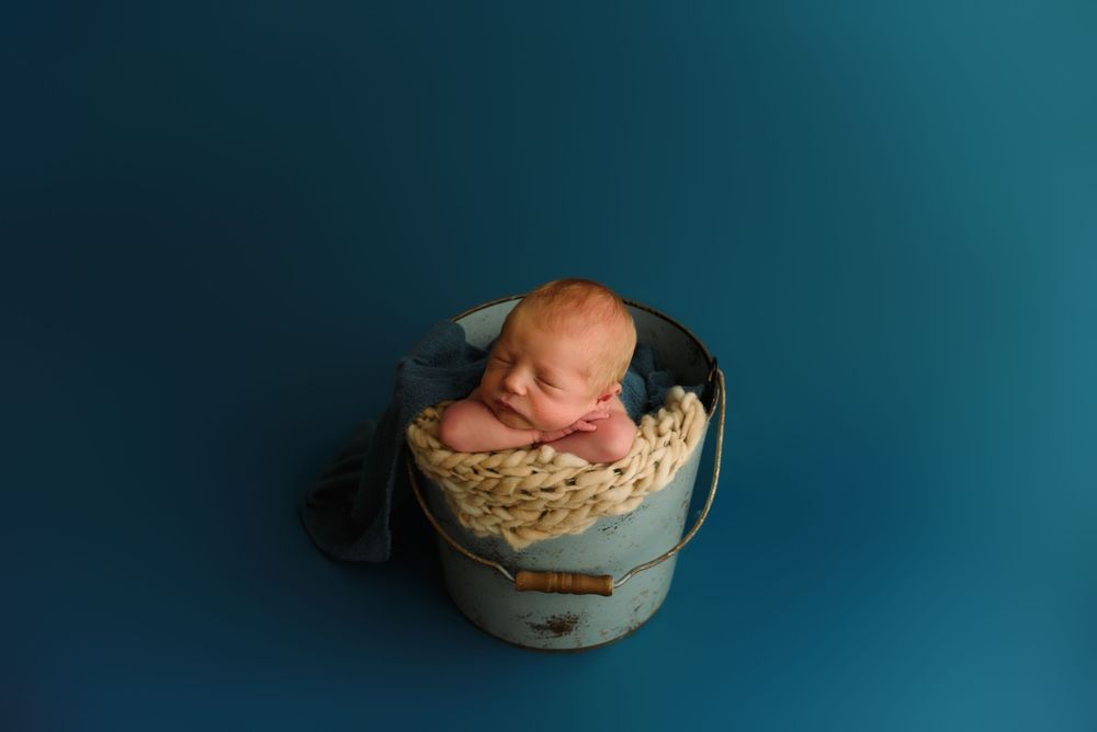 Peaceful newborn sleeping in blue vintage container against teal backdrop.