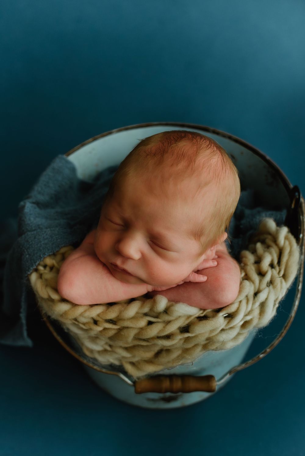 Sleeping newborn baby nestled in cozy woven basket against dark blue backdrop.