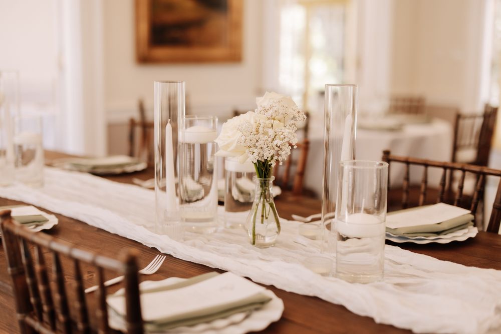 Elegant table setting with white hydrangeas in glass vase, tall candlesticks, and brown Chiavari chairs at a wedding reception.
