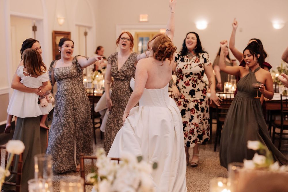Wedding reception guests dancing and enjoying festivities in a brightly lit venue with floral decorations.