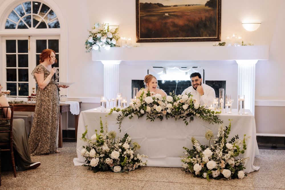 Elegant wedding reception venue with white floral arrangements and decorative lighting in a classic white room.