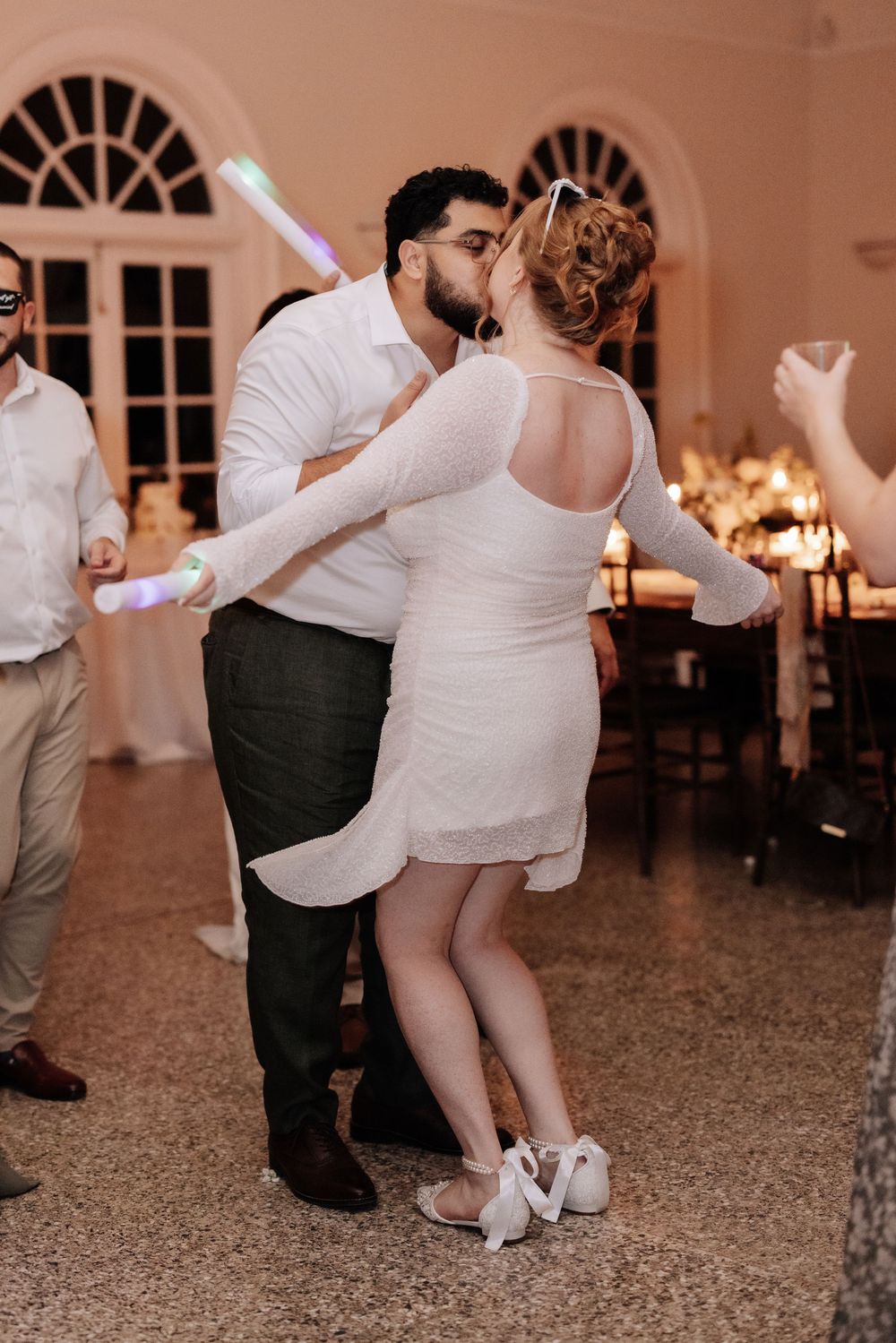 Wedding guests dance energetically on the dance floor in white shirts and formal attire at an elegant indoor reception.