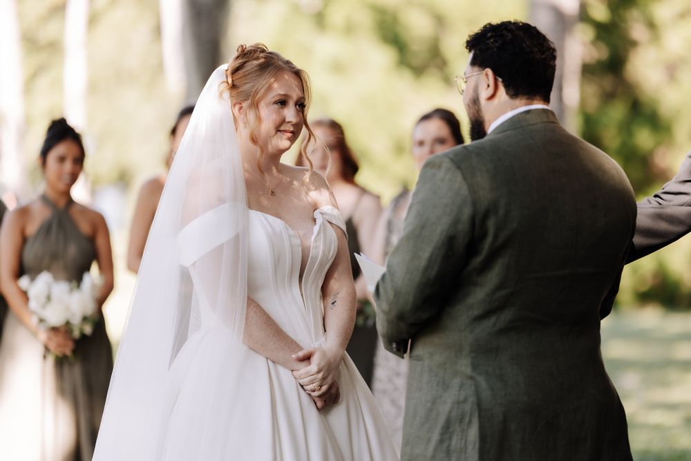 Wedding party in formal attire walks through a sunlit garden during an outdoor ceremony.
