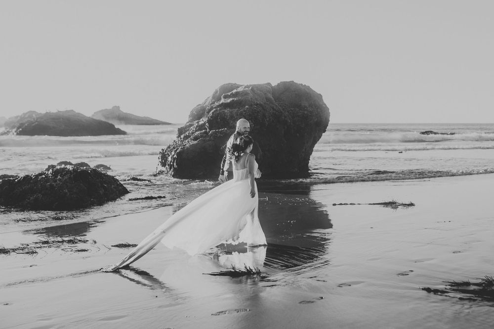 A scenic black and white photograph shows waves crashing against rocky outcrops along a misty Pacific coast beach.