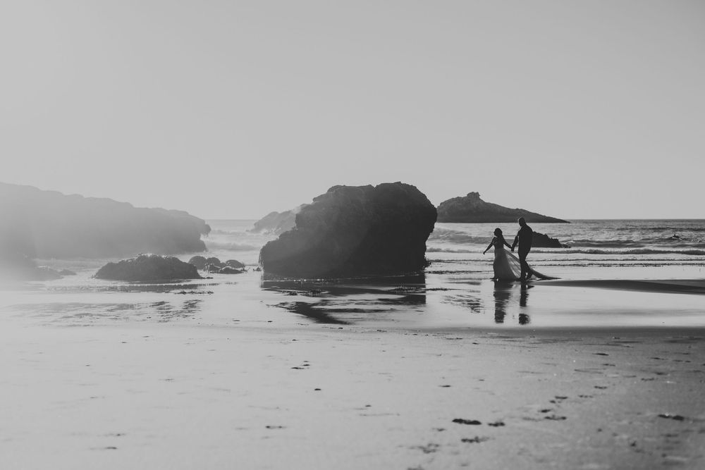 A series of black and white photographs showing figures walking along a misty beach with dramatic coastal rock formations.
