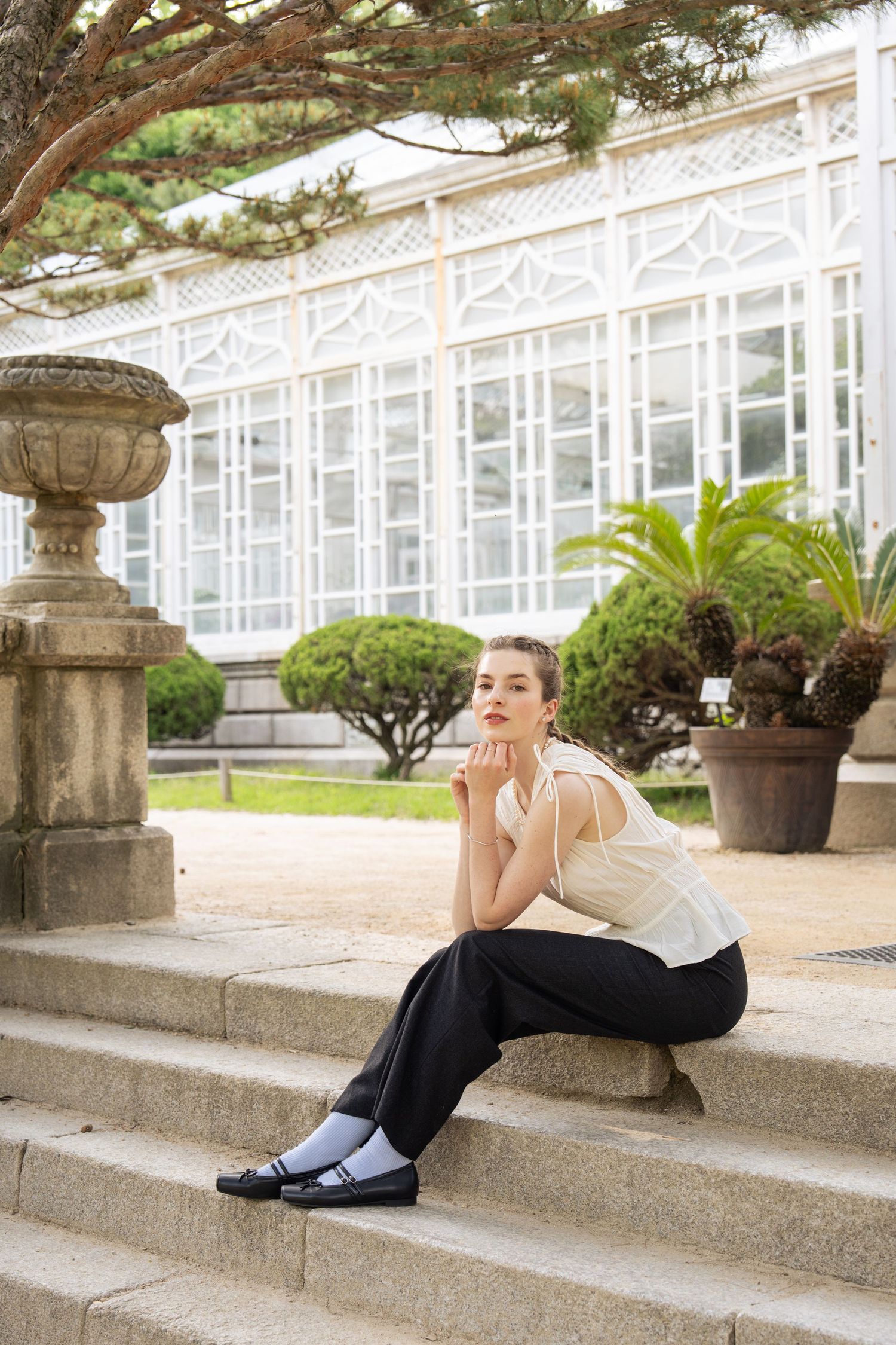 A person in athletic wear rests on concrete steps near ornate white architecture and garden planters.