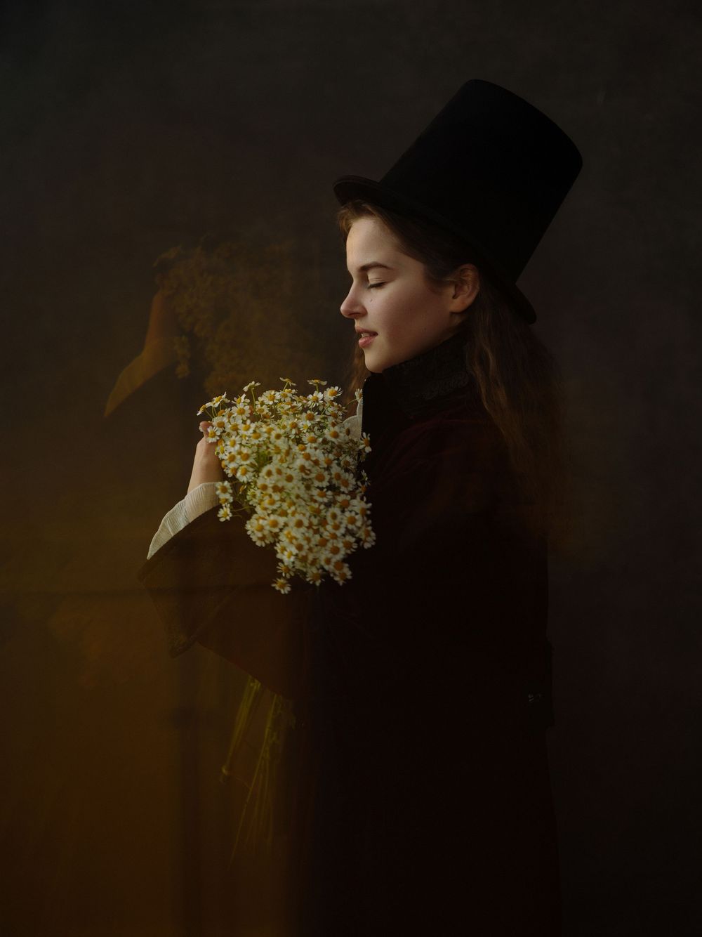 A woman in a dark coat and top hat holds white wildflowers, eyes closed, against a moody dark background.