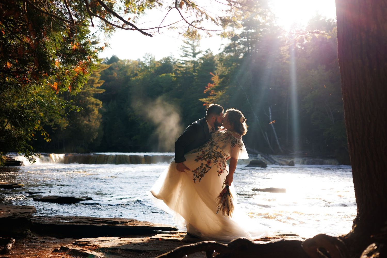 A romantic sunset photoshoot at a serene lake with sunbeams streaming through trees and silhouettes against golden light.