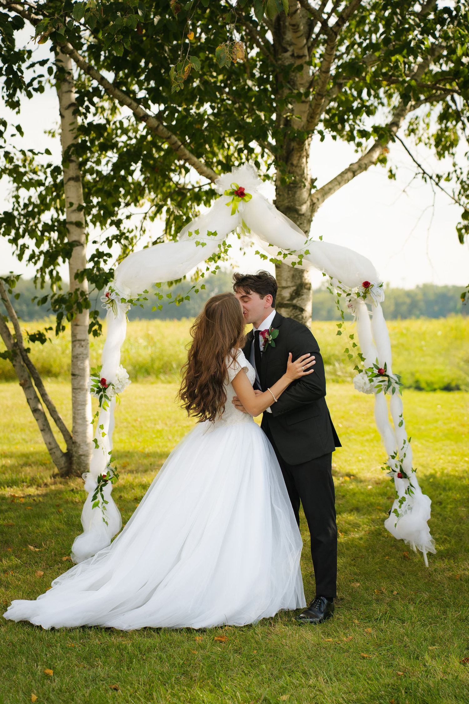 Close-up of intertwined hands wearing wedding rings with burgundy floral bouquet.