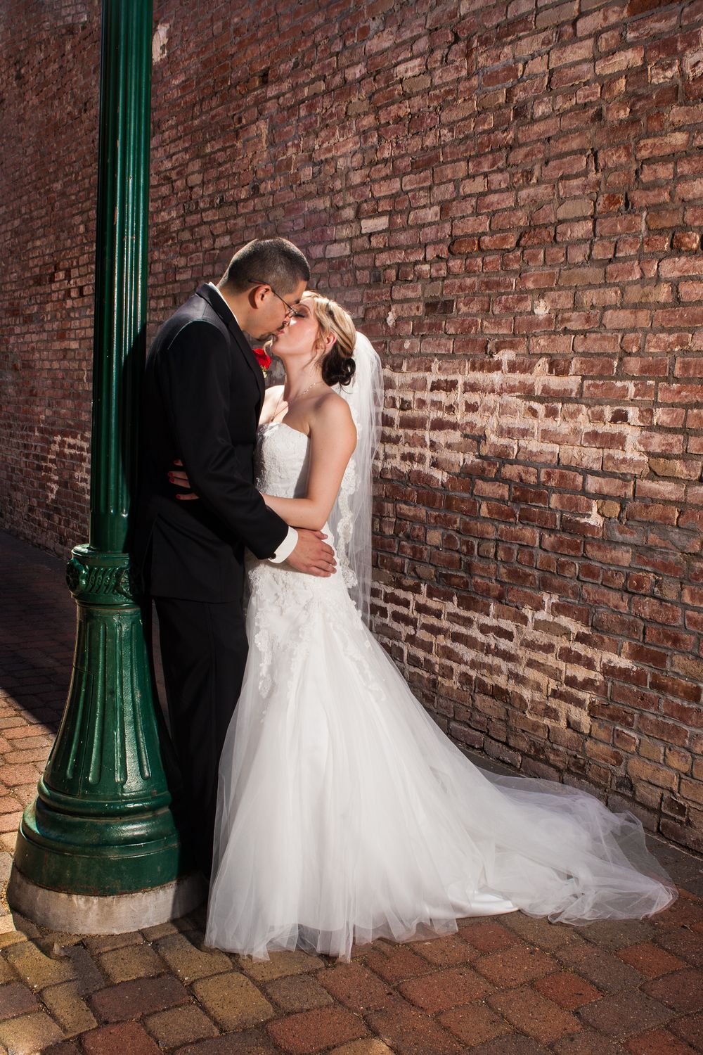 A romantic wedding photo sequence showing a couple embracing near a vintage green lamp post against a brick wall.