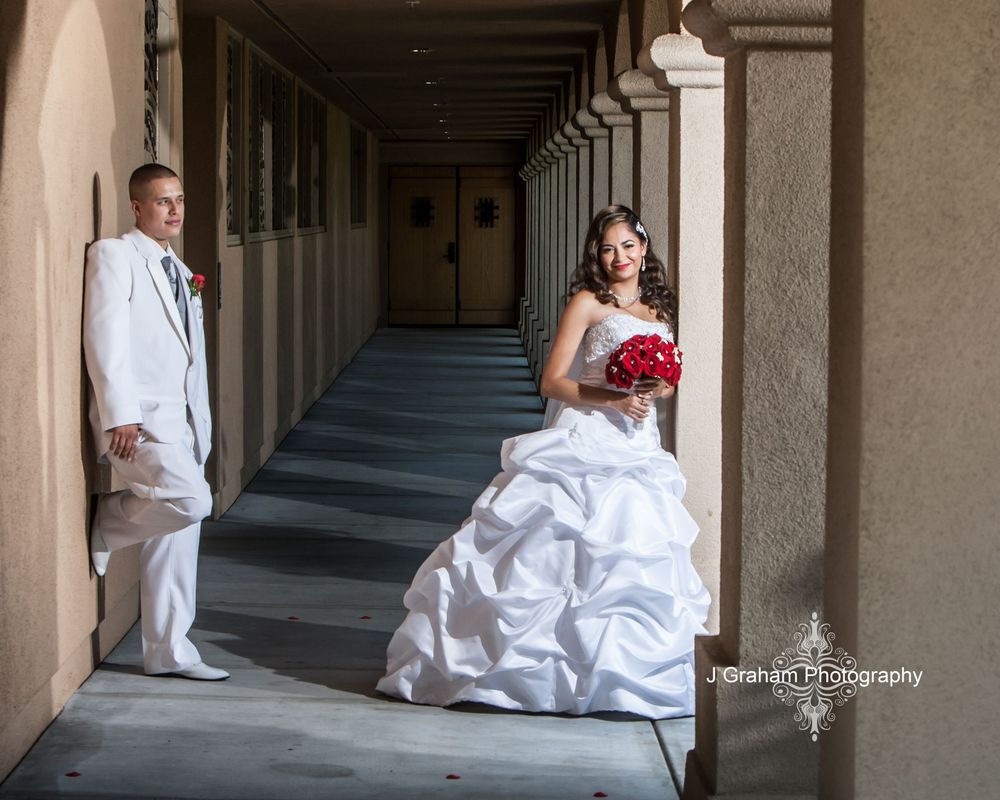 A panoramic wedding photo showing a couple in white sitting along a stone colonnade walkway.