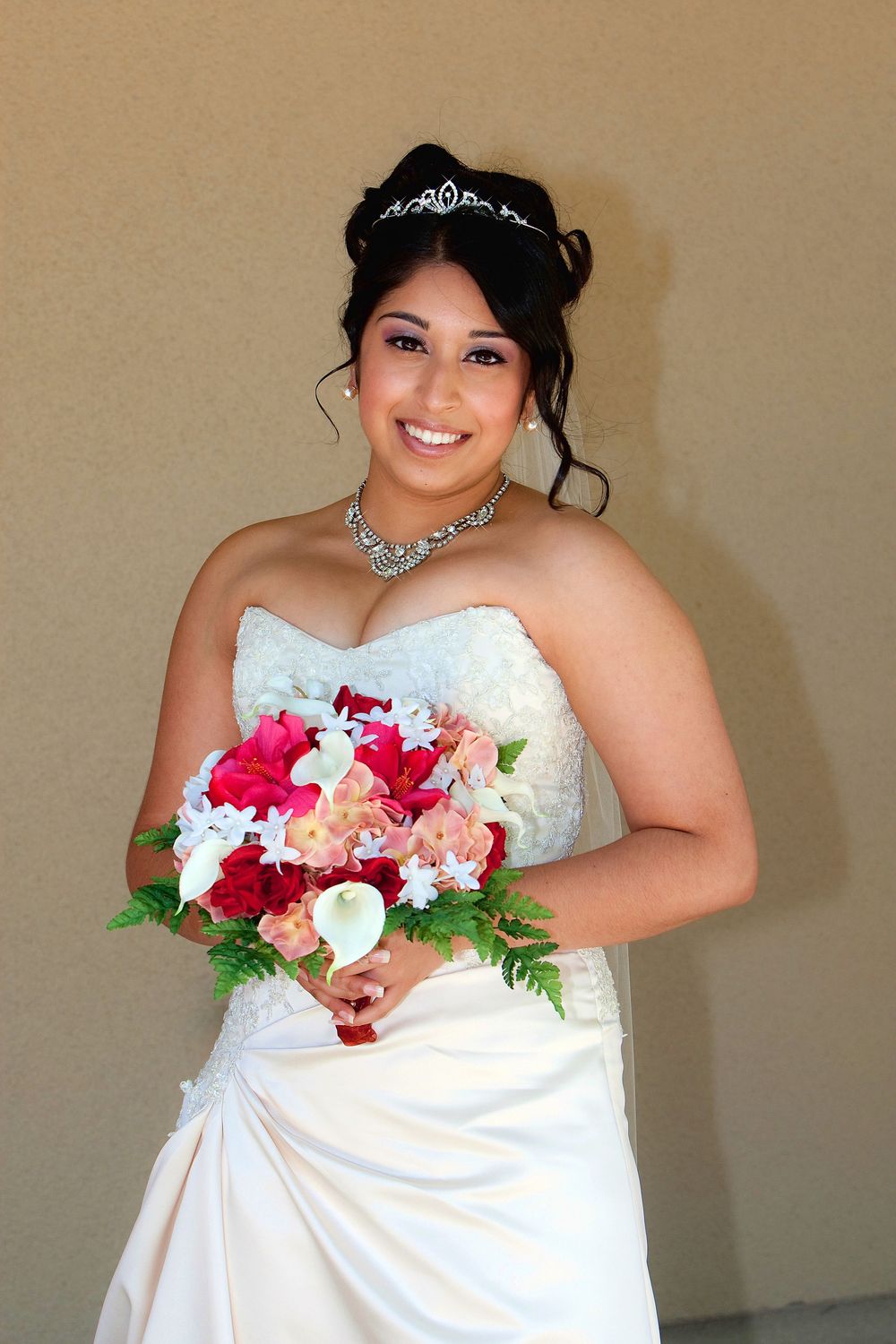 A bride in a white strapless wedding dress holds a vibrant bouquet of red and pink flowers.
