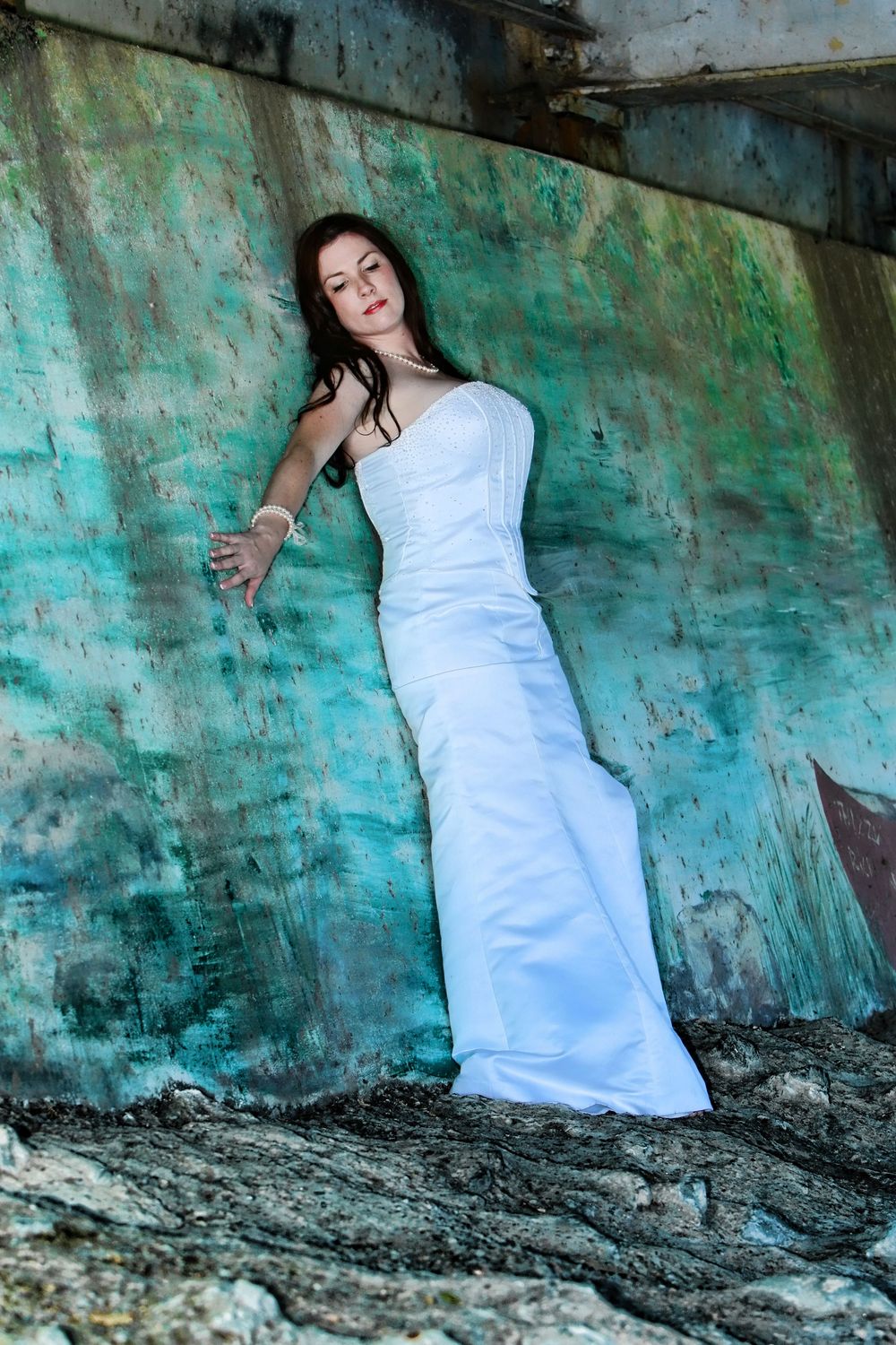 A woman in a white dress poses dramatically against a weathered turquoise wall in a photo series.