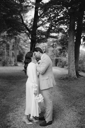 Romantic black and white photo of a couple in formal wear embracing outdoors.