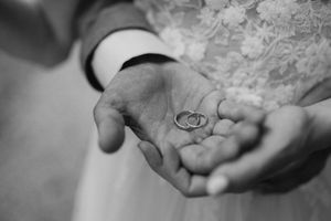 Close-up of hands holding wedding rings against a textured background.